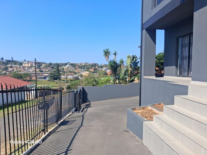 Exterior view of the property entrance featuring a paved driveway, metal security fencing, and tiled steps leading to the main entrance.