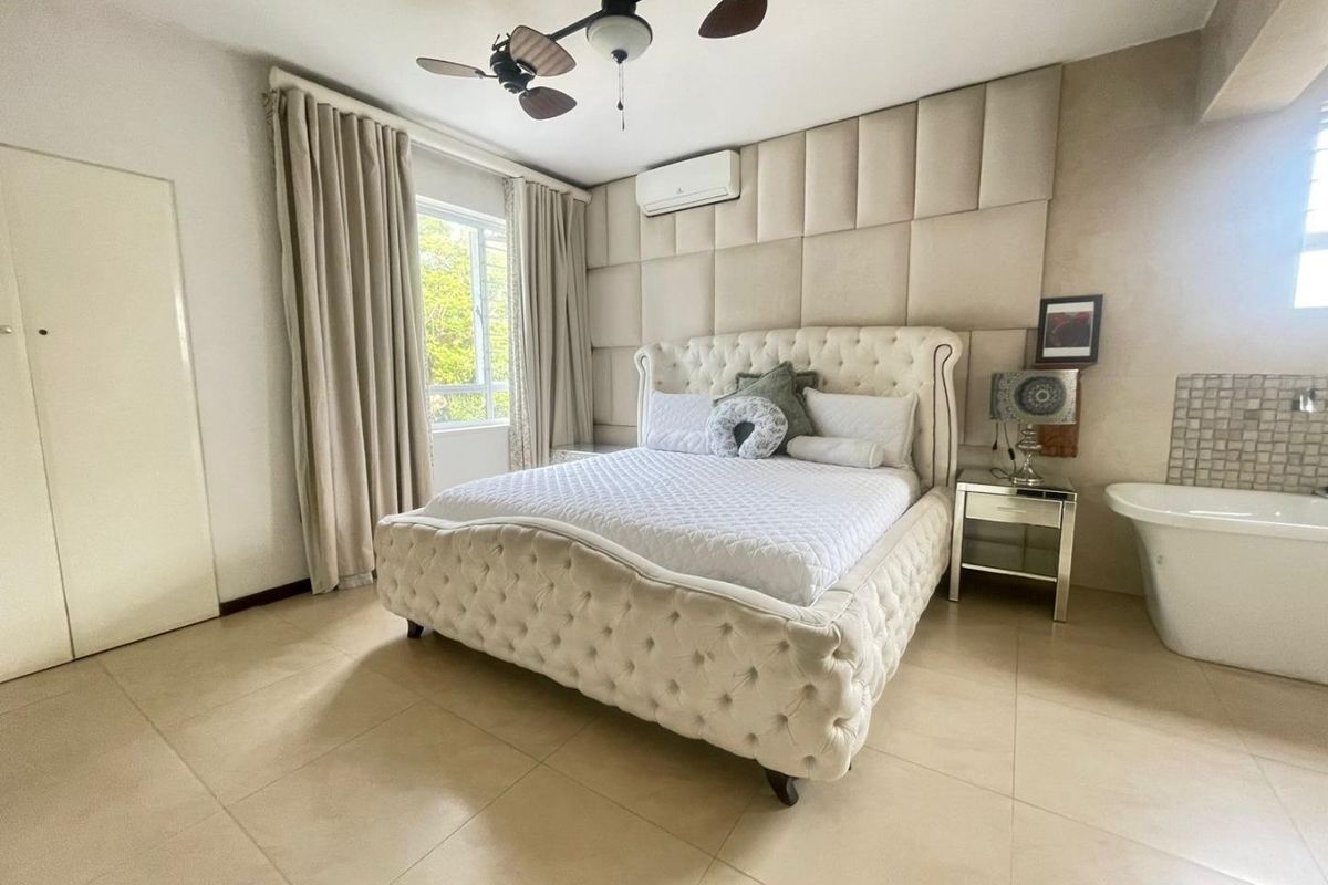 Spacious bedroom featuring upholstered wall paneling, tiled flooring, a ceiling fan, split-system air conditioning, and an integrated freestanding bathtub.