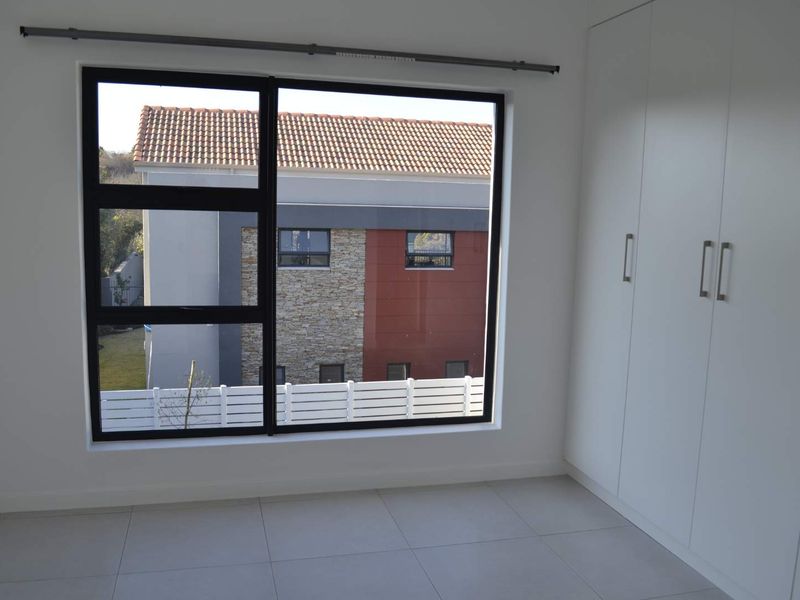 A bright, empty bedroom featuring modern tiled flooring, built-in cupboards, and a large window with an aluminium frame.