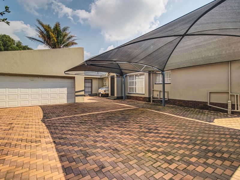 Front exterior view featuring a paved driveway, a large shade sail carport, and a secure garage entrance.