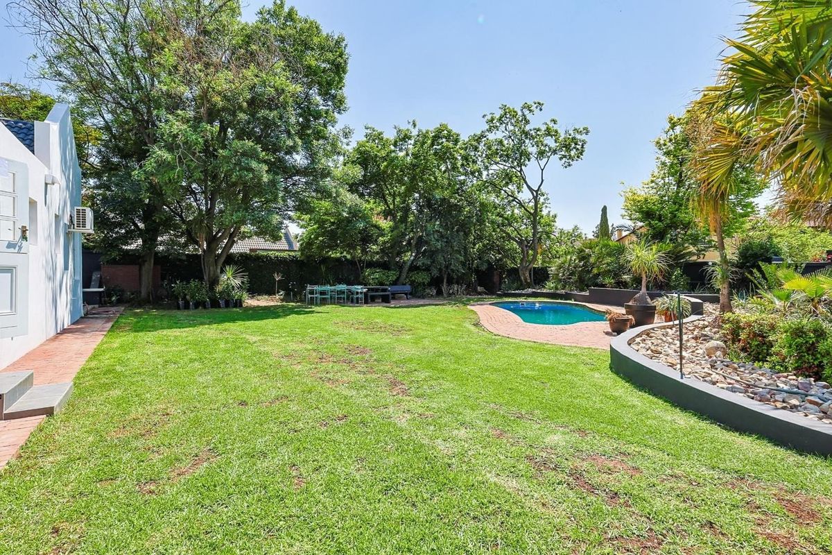 Spacious rear garden featuring a well-maintained lawn, mature trees, and a swimming pool with a paved surround.