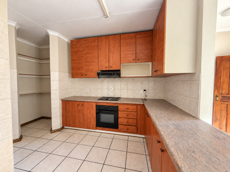 A functional kitchen featuring wood-finish cabinetry, built-in oven and hob, tiled backsplash, and a convenient open-shelving pantry area.