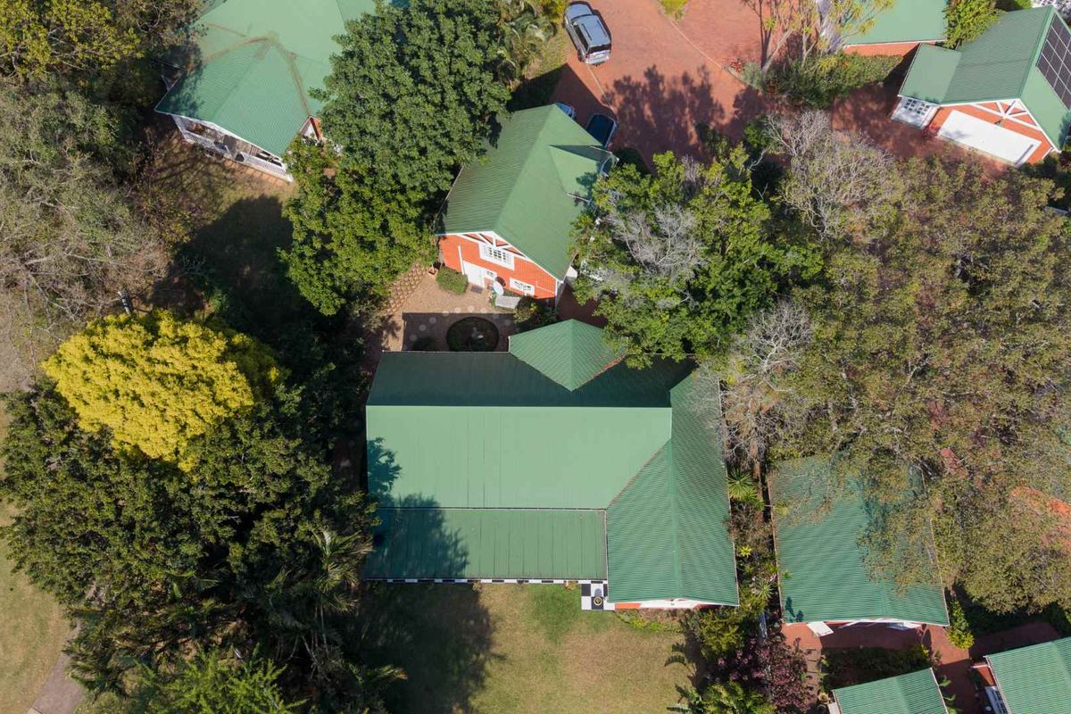 Aerial view of a residential property featuring green metal roofing, paved driveway access, and established garden surroundings within a suburban estate.