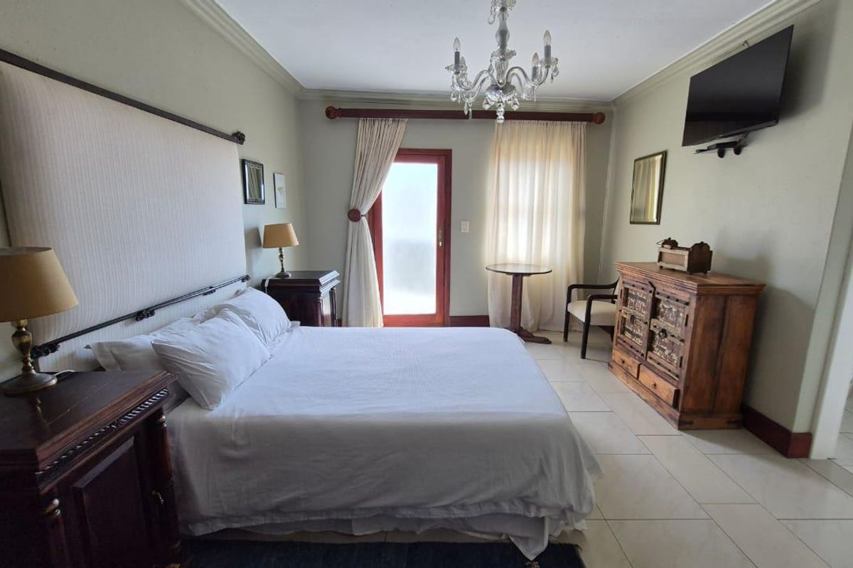 A spacious bedroom featuring tiled flooring, a built-in headboard, and direct access to an outdoor area through a glass-paneled door.