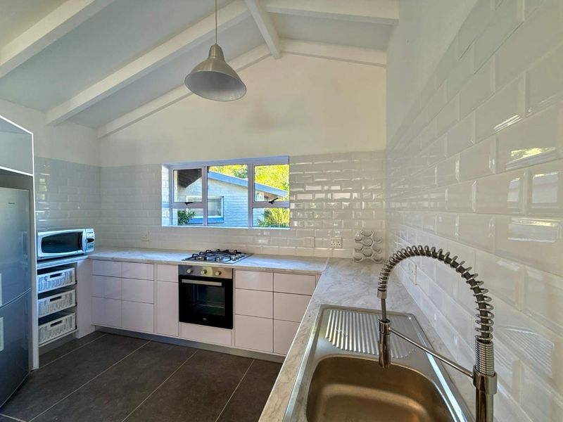 Modern kitchen featuring white cabinetry, subway tile backsplash, marble-look countertops, stainless steel appliances, and an exposed beam ceiling with ample natural light.