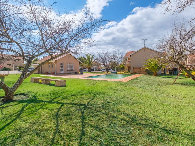 A communal outdoor area featuring a swimming pool, brick paved surround, and well-maintained lawn within an apartment complex setting.
