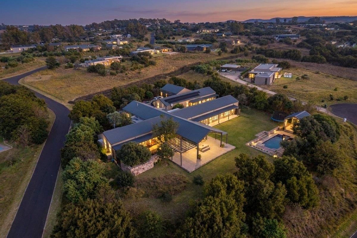 Aerial view of a modern residential property featuring a cross-shaped architectural design, metal roofing, a swimming pool, and a covered patio area.