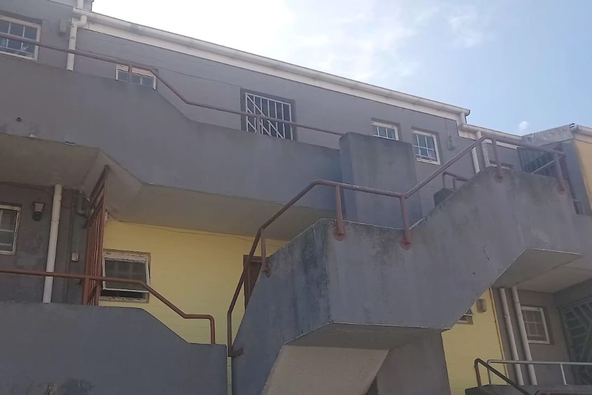 Rear exterior view of an apartment building featuring an external concrete staircase, balconies, and security-fitted windows with visible signs of weathering.