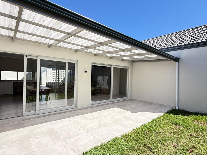A modern covered patio featuring tiled flooring and a translucent roof, providing seamless indoor-outdoor flow through large sliding glass doors.