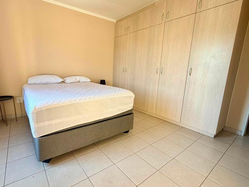 A bedroom featuring light-toned built-in cupboards and neutral tiled flooring, providing a functional and clean living space.