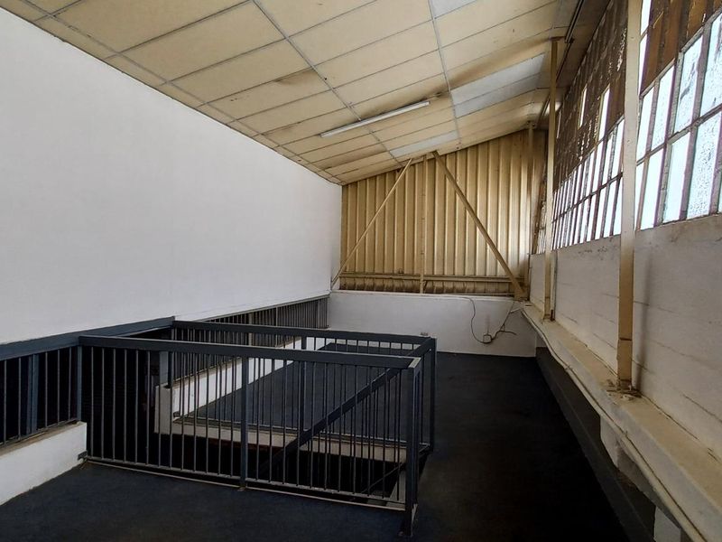 An industrial mezzanine level featuring metal safety railings, corrugated wall cladding, and large industrial windows, providing an open, functional utility space.