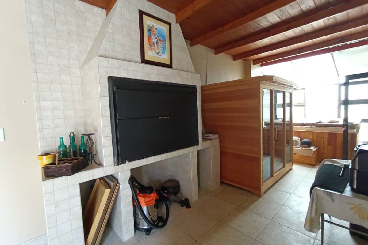 An indoor entertainment area featuring a large built-in tiled fireplace and a wooden sauna unit, with exposed timber ceiling beams and tiled flooring.