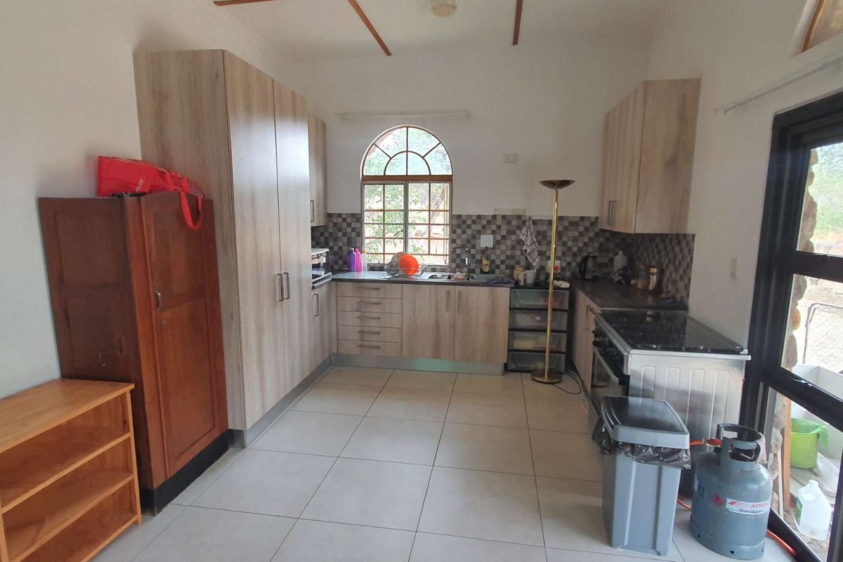 A functional kitchen featuring light wood-grain cabinetry, tiled splashbacks, a built-in oven, and an arched window providing natural light.