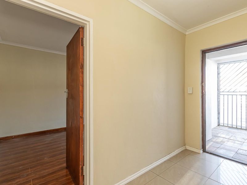 A clean, empty hallway featuring tiled flooring, connecting to a bedroom with laminate flooring and an exterior door with a security gate.