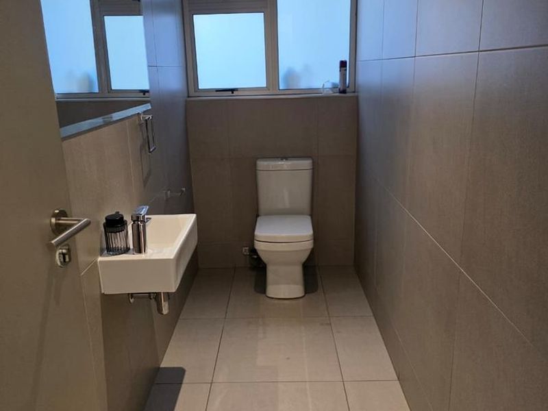 A modern, minimalist guest bathroom featuring neutral floor-to-ceiling wall tiles, a wall-mounted basin, and a clean, contemporary toilet.