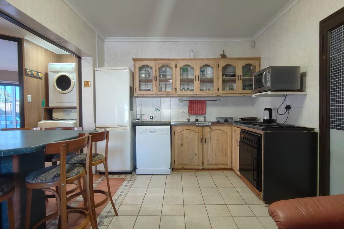 A functional kitchen featuring wooden cabinetry, tiled flooring, and a breakfast bar, with an adjacent laundry area visible.