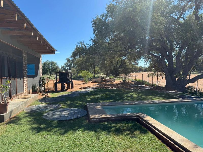Outdoor pool area featuring a swimming pool with stone coping, adjacent to a covered patio with exposed timber rafters and brick wall construction.