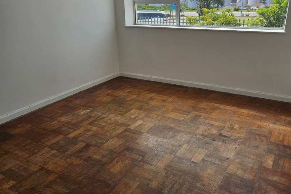 An empty bedroom featuring original parquet flooring and a large window with an exterior view.