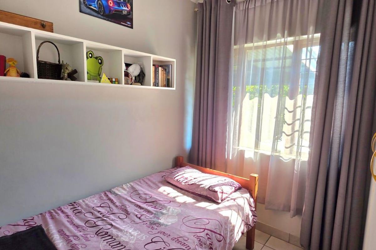 A cozy bedroom featuring tiled flooring, built-in wall shelving, and a window dressed with curtains.