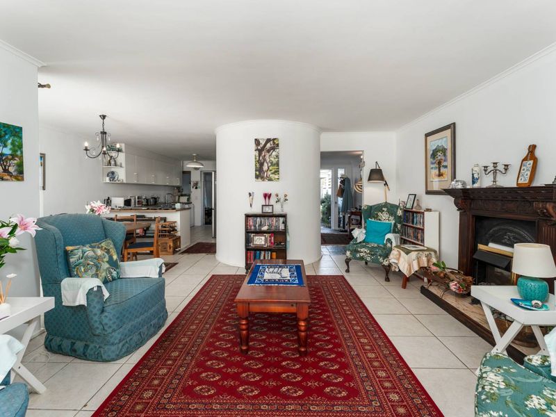 An open-plan living and kitchen area featuring tiled floors, a central curved structural column, and a traditional fireplace mantel.