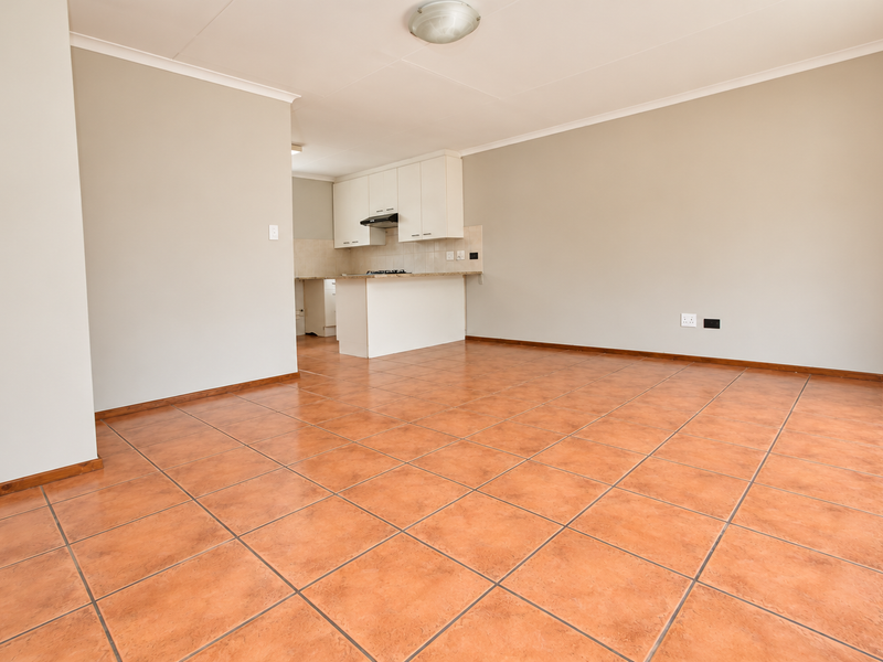 An open-plan living and kitchen area featuring terracotta-style floor tiles, neutral walls, and a compact kitchen with built-in cabinetry and a hob.