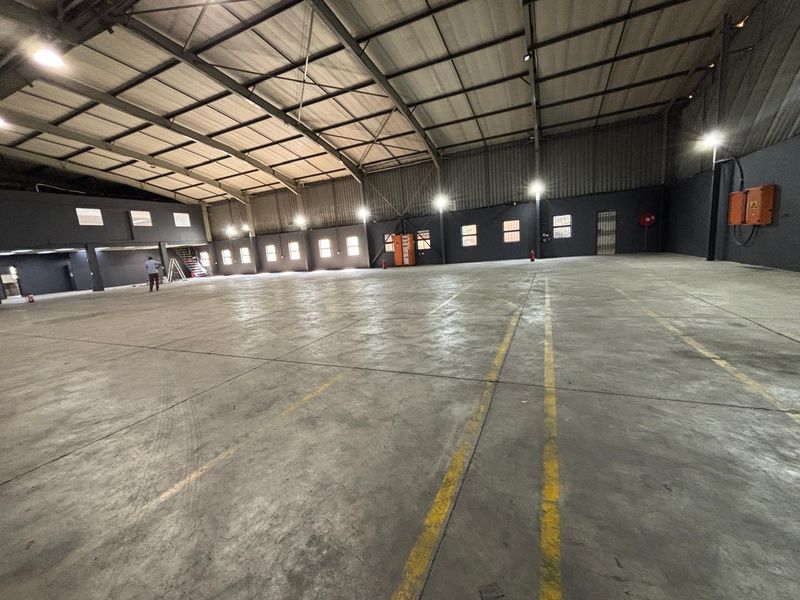 Spacious industrial warehouse featuring high ceilings, exposed steel trusses, polished concrete flooring, and functional industrial lighting throughout the open floor plan.