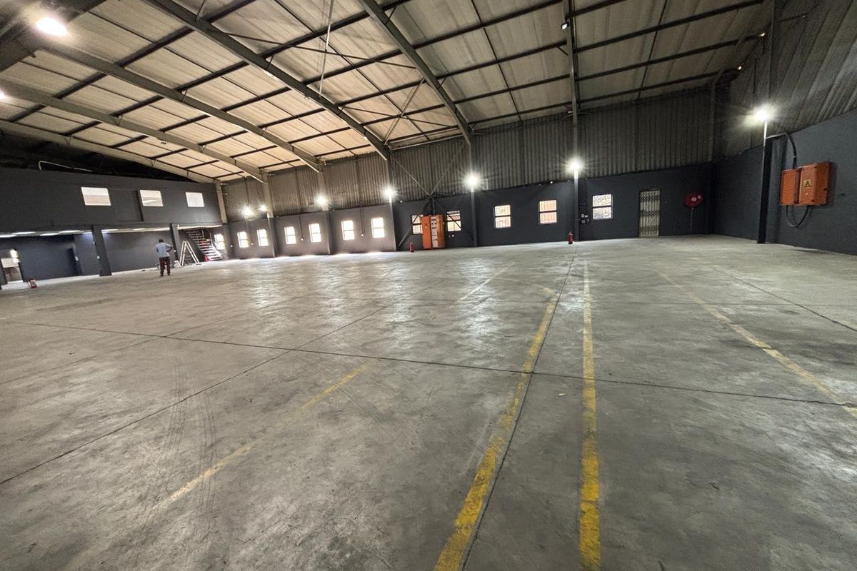 Spacious industrial warehouse featuring high ceilings, exposed steel trusses, polished concrete flooring, and functional industrial lighting throughout the open floor plan.