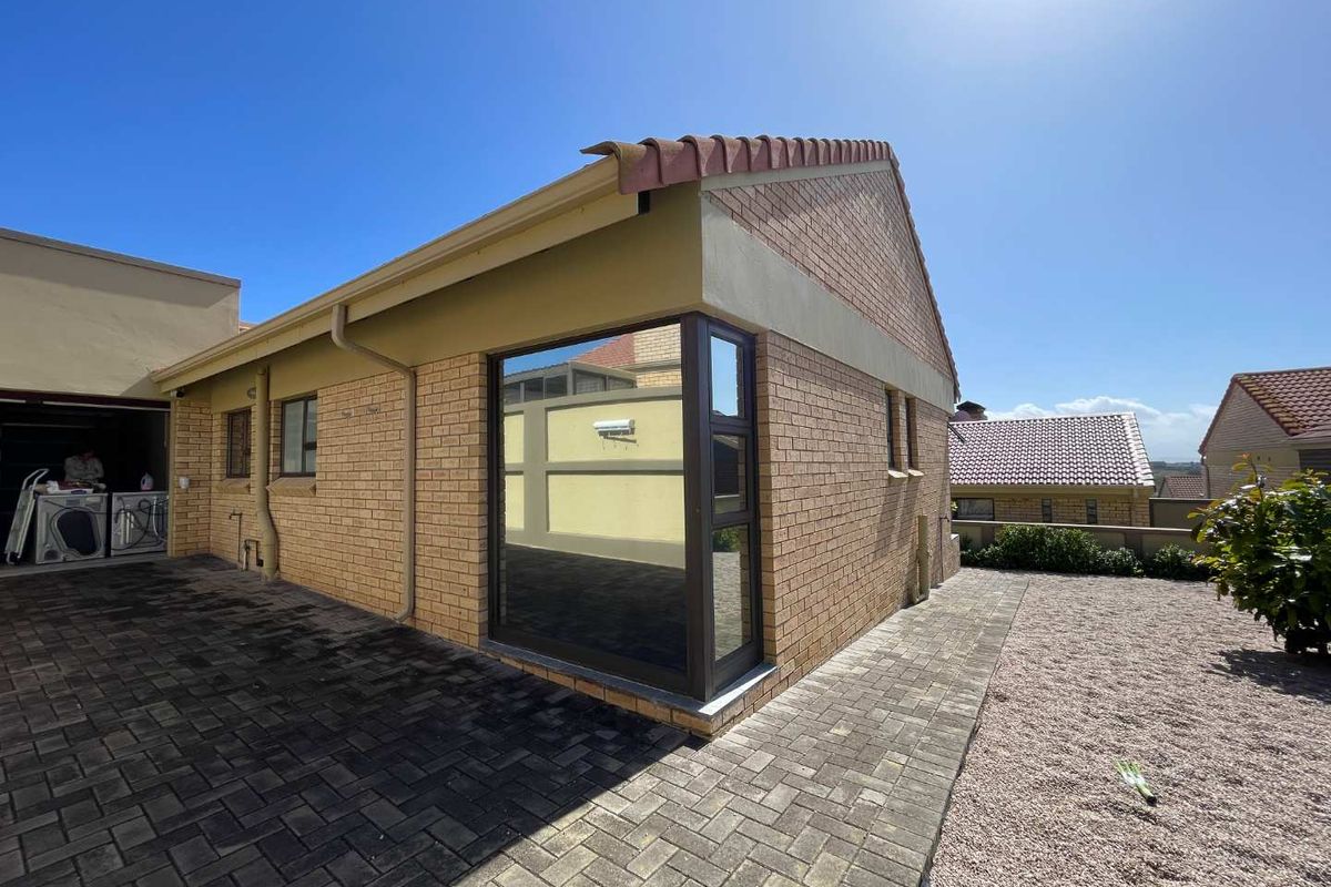 Rear view of the property featuring a brick facade, tiled roof, corner window, and paved patio area.