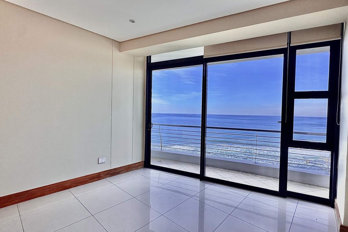 Bright, empty living space featuring large sliding glass doors that open onto a balcony with expansive ocean views.