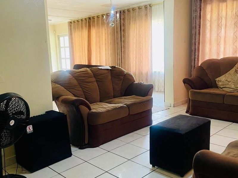 A spacious living area featuring neutral ceramic floor tiles and a large opening leading to an adjacent room with natural light.
