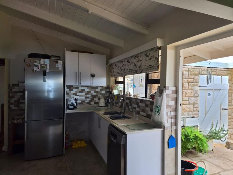 A functional kitchen featuring white cabinetry, a tiled backsplash, and a double sink, with direct access to an outdoor patio area.