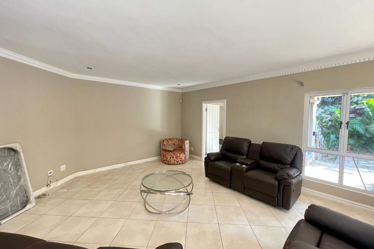 Spacious living room featuring neutral tiled flooring, decorative ceiling cornicing, and large windows providing natural light and garden views.