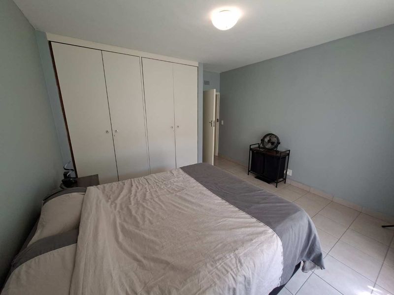 A functional bedroom featuring built-in cupboards, neutral wall tones, and tiled flooring, offering a clean and practical living space.