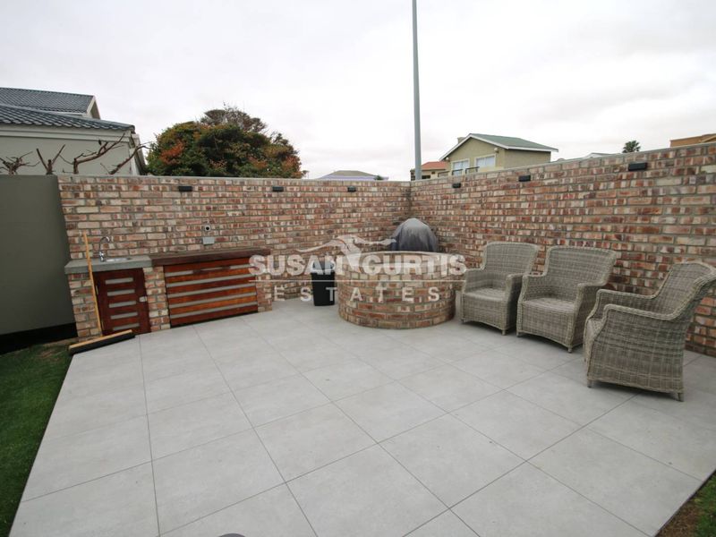Outdoor patio area featuring a built-in braai, integrated sink, and brick boundary wall, finished with modern floor tiles.