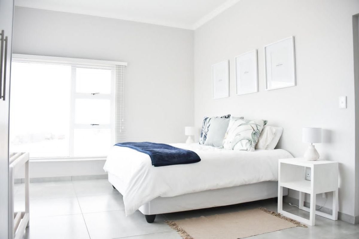 A bright and modern bedroom featuring neutral tones, large windows for natural light, and clean tiled flooring.