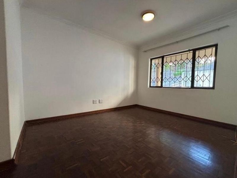 A bright, empty bedroom featuring classic parquet flooring, neutral walls, and security bars on the window, providing a clean canvas for personalization.
