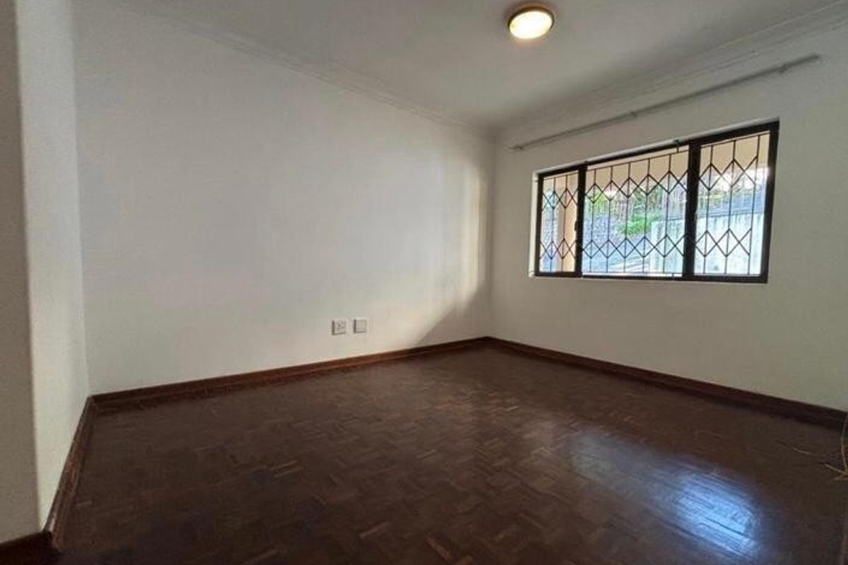 A bright, empty bedroom featuring classic parquet flooring, neutral walls, and security bars on the window, providing a clean canvas for personalization.