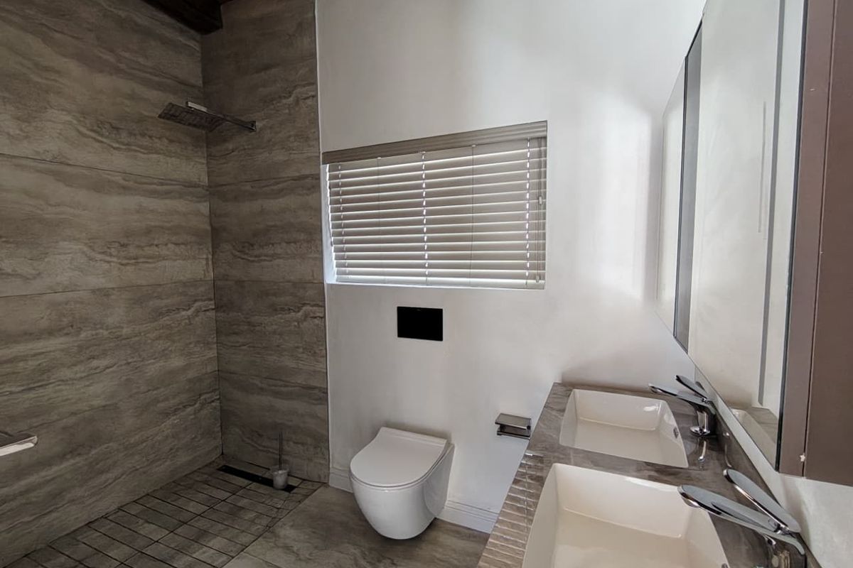Modern bathroom featuring a spacious walk-in shower with rain head, wall-hung toilet, and a sleek double vanity with contemporary fixtures.