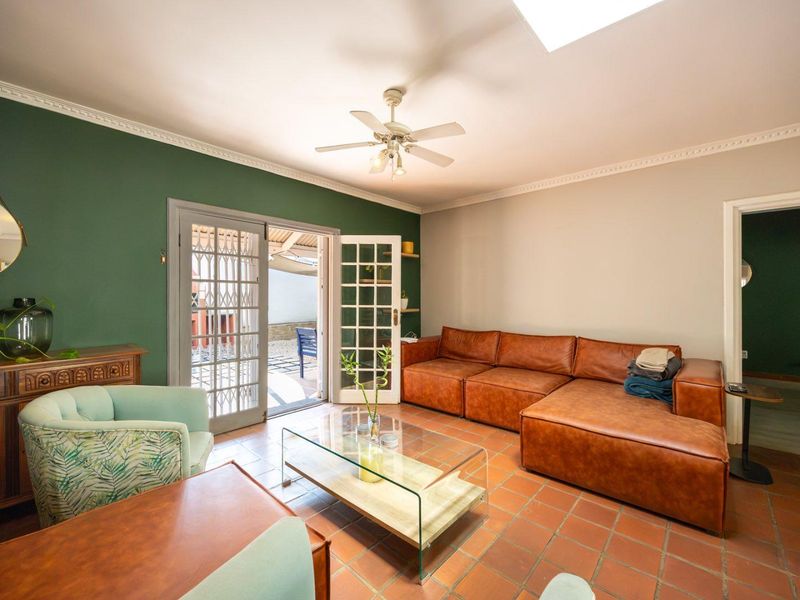 A cozy living room featuring terracotta floor tiles, a ceiling fan, crown molding, and direct access to an outdoor patio through classic french doors.