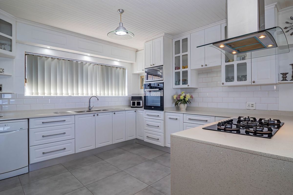 Modern, well-appointed kitchen featuring white cabinetry, stone countertops, subway tile backsplash, and high-quality built-in appliances including a gas hob and oven.