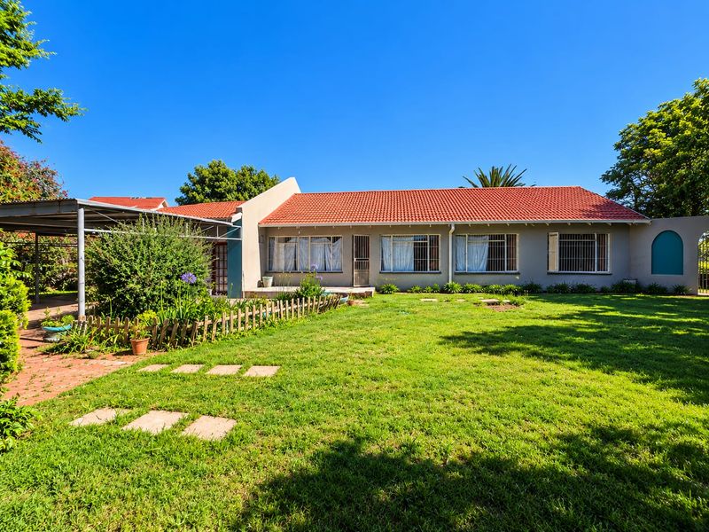 Rear view of the house featuring a terracotta tiled roof, a covered patio area, and a well-maintained garden with a paved walkway.