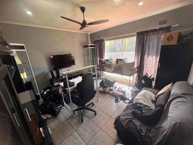 A living room featuring tiled flooring, a ceiling fan, and recessed downlights, offering a functional space with natural light from a large window.