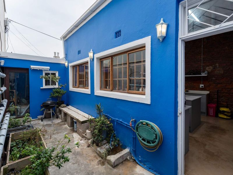A rear courtyard area featuring vibrant blue exterior walls, timber-framed windows, and direct access to an interior space with exposed brick finishes.