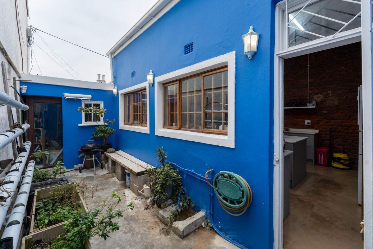 A rear courtyard area featuring vibrant blue exterior walls, timber-framed windows, and direct access to an interior space with exposed brick finishes.