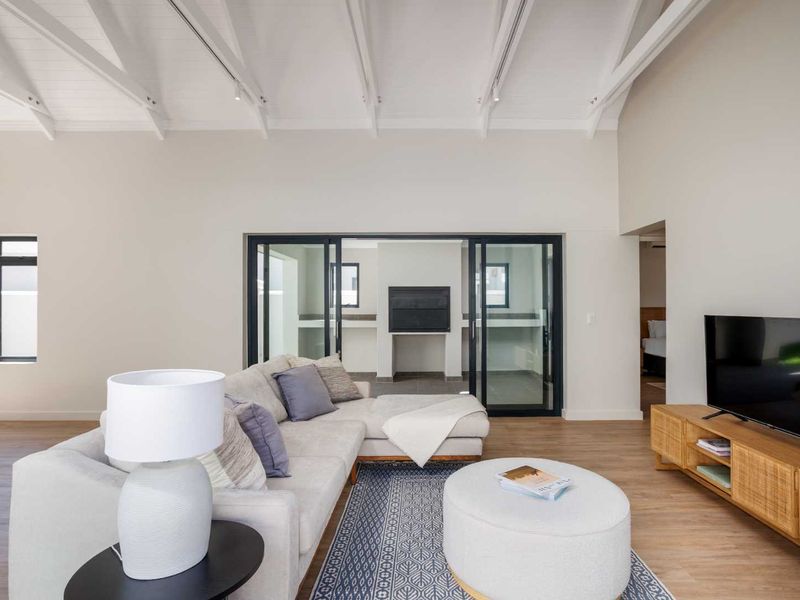 Spacious living room featuring vaulted ceilings with exposed rafters, modern laminate flooring, and large sliding glass doors leading to an outdoor area with a fireplace.
