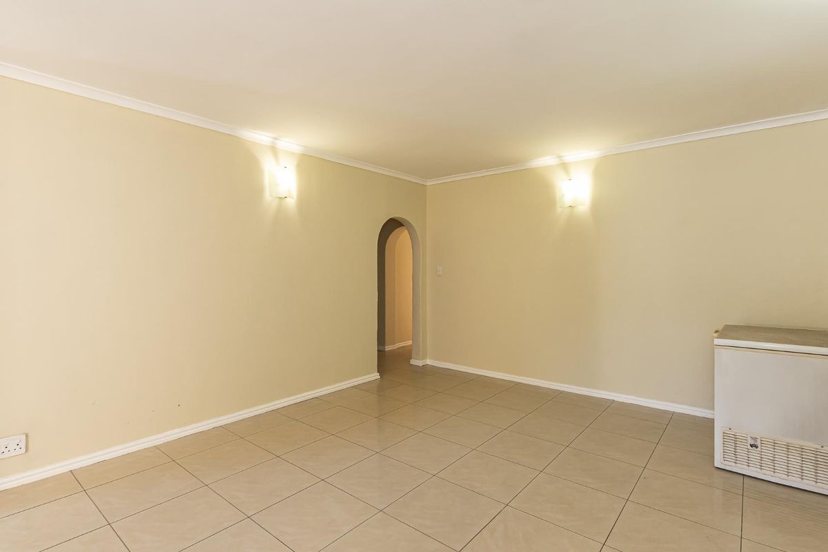 A spacious, empty living area featuring neutral tiled flooring, coving, and a distinctive arched doorway leading to an adjacent room.