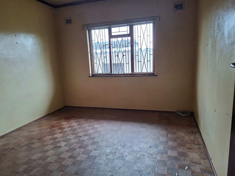 An empty bedroom featuring original parquet flooring, security bars on the window, and walls in need of cosmetic refurbishment.