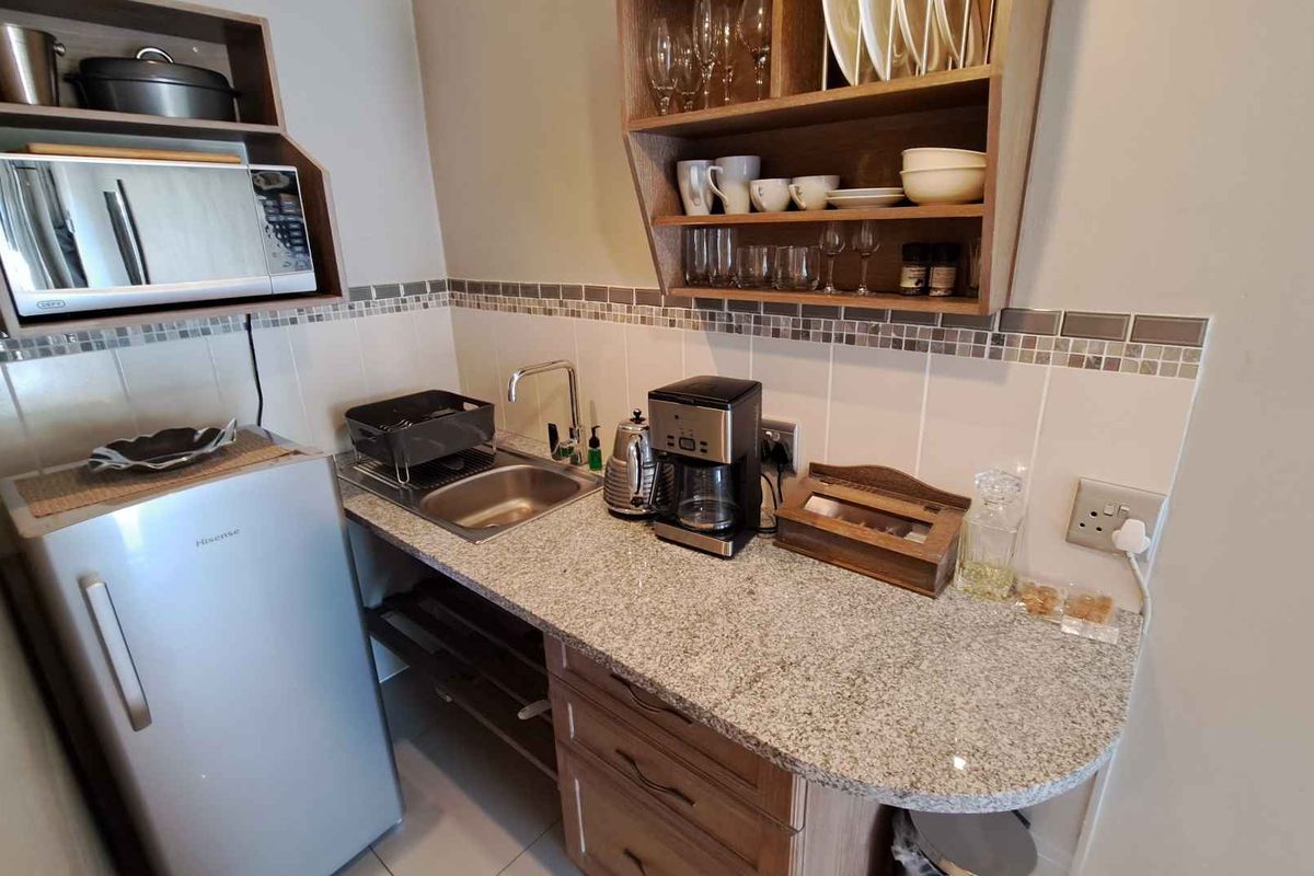 Compact kitchenette featuring granite countertops, built-in cabinetry, open shelving, a stainless steel sink, and tiled backsplash.