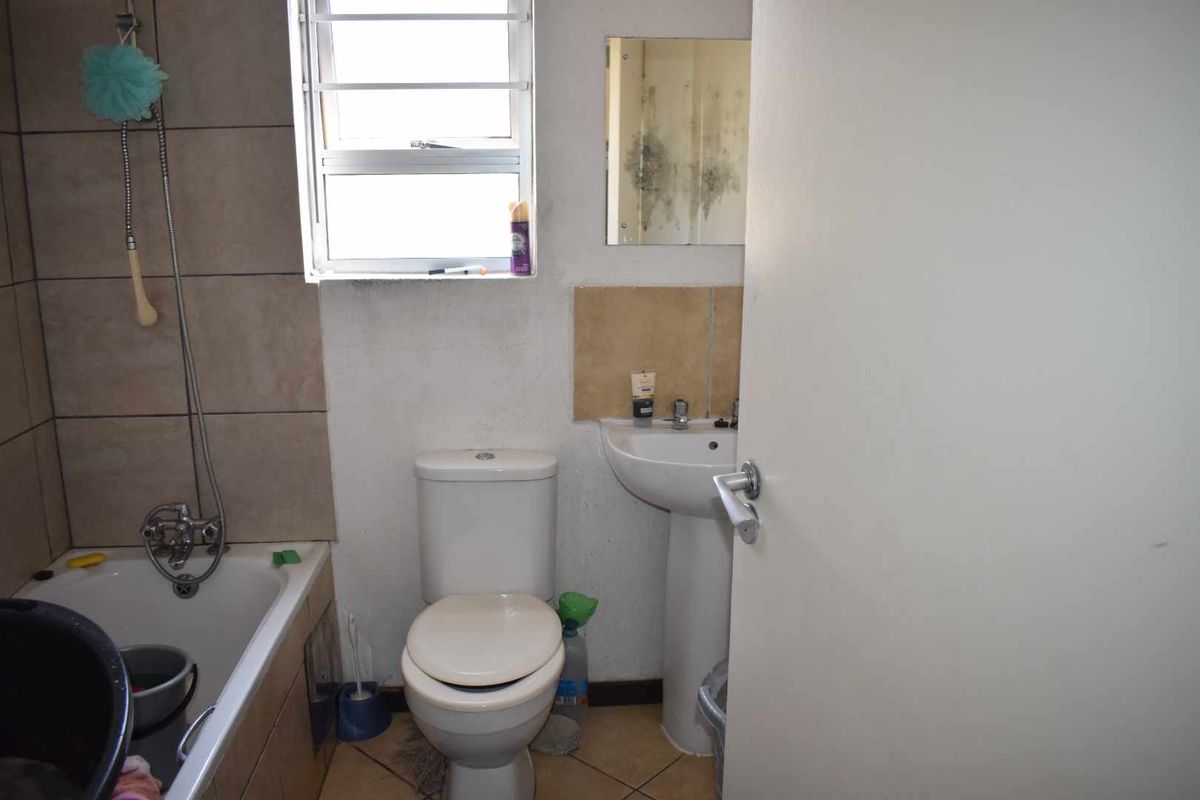 A compact bathroom featuring a bathtub with shower attachment, pedestal basin, and toilet, requiring maintenance and cosmetic updates to address wall damage and mold.