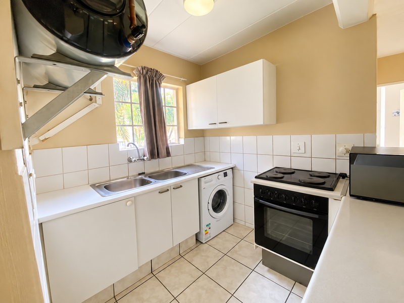 Functional kitchen featuring white cabinetry, tiled backsplash, stainless steel sink, and a built-in electric stove and oven.
